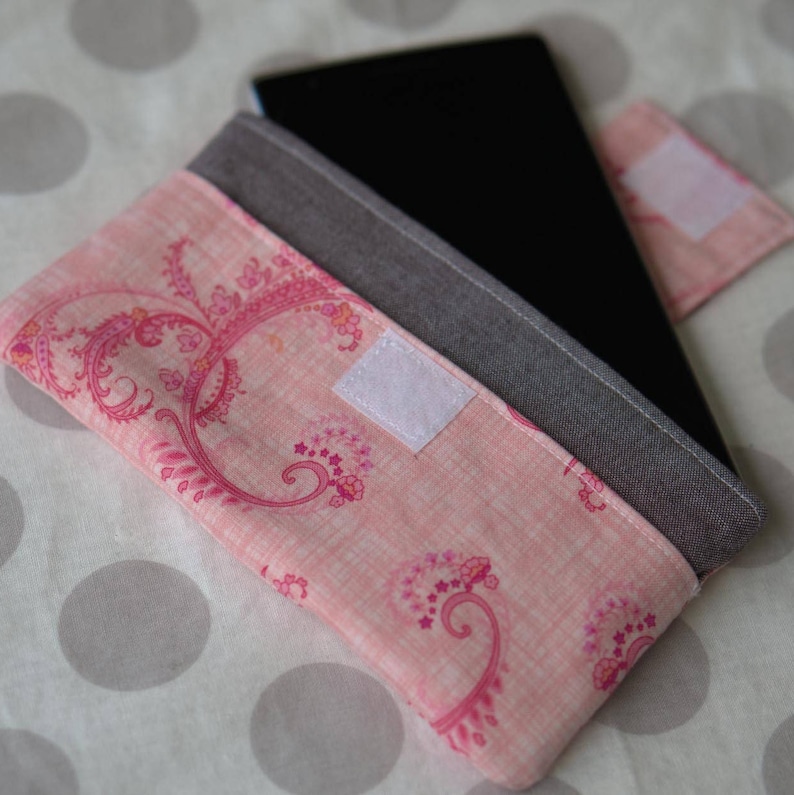 May include: A pink fabric tablet case with a paisley pattern and a gray fabric flap. The case has a white velcro closure.