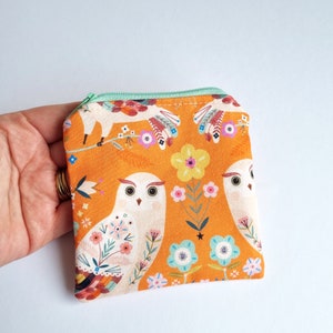 May include: A small orange zippered pouch with a white owl and floral pattern. The owl has large eyes and a detailed design.