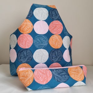 May include: A teal blue fabric tote bag with a zipper closure and a matching teal blue fabric pouch. The bag and pouch are decorated with a repeating pattern of colorful yarn balls.