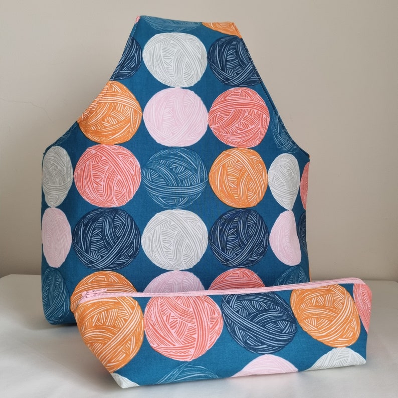 May include: A teal blue fabric tote bag with a zipper closure and a matching teal blue fabric pouch. The bag and pouch are decorated with a repeating pattern of colorful yarn balls.