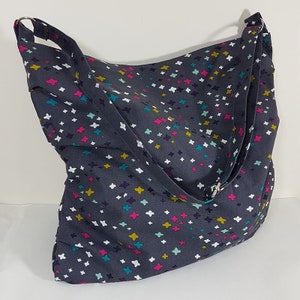 Peut inclure: Un sac fourre-tout en tissu gris avec un motif d'étoiles colorées. Le sac a une longue bandoulière et une fermeture à glissière.