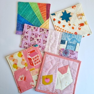 Puede incluir: Conjunto de seis posavasos de tela coloridos con varios patrones, que incluyen un arcoíris, gatos, una caja de leche y una estrella. Los posavasos están hechos de tela de patchwork y son perfectos para proteger las superficies del calor y los derrames.