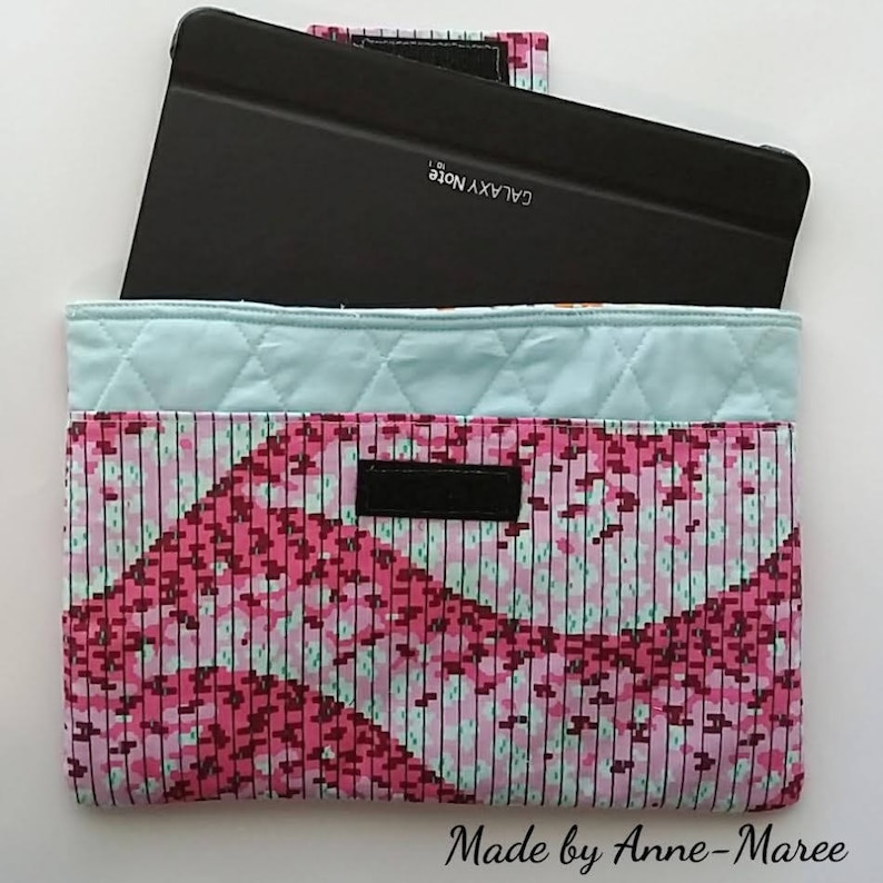 Puede incluir: Una funda acolchada para tablet con un patr&oacute;n geom&eacute;trico rosa y azul. La funda est&aacute; abierta y una tablet negra con el texto "GALAXY NOTE" est&aacute; dentro.