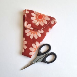 May include: A red and pink floral fabric scissor case with a snap closure and a pair of small silver scissors.