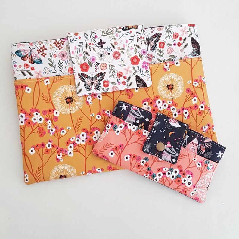 May include: Three fabric pouches with floral patterns. The largest pouch is yellow with white flowers and a butterfly design. The medium pouch is white with pink and red flowers and a butterfly design. The smallest pouch is pink with white flowers and a black and white design.