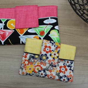 Puede incluir: Dos bolsas de tela con diferentes patrones. La primera bolsa es negra con una solapa rosa y un estampado de c&oacute;cteles coloridos. La segunda bolsa es amarilla con un estampado floral blanco y negro.