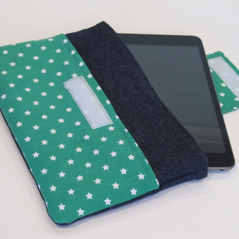May include: A green fabric tablet case with white stars and a denim flap. The case has a velcro closure and a white velcro strip on the front.