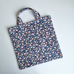 May include: A small blue tote bag with a floral print featuring pink, orange, and white flowers on a dark blue background.