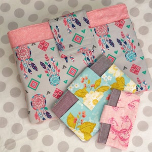 Puede incluir: Cuatro bolsas de tela con diferentes patrones. La bolsa m&aacute;s grande es gris con ribete rosa y presenta un dise&ntilde;o de atrapasue&ntilde;os. Las otras bolsas son m&aacute;s peque&ntilde;as y presentan patrones florales y paisley.