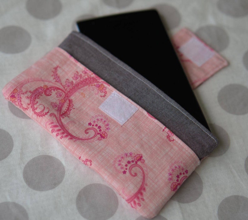 Puede incluir: Una funda para tablet de tela rosa con una solapa de tela gris y un patr&oacute;n floral. La funda tiene un cierre de velcro blanco.