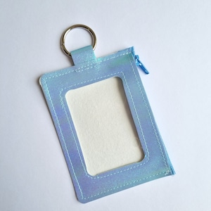 May include: A light blue iridescent zippered pouch with a clear plastic window and a silver key ring.