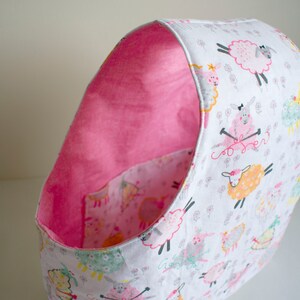 May include: A pink and white fabric storage bin with a sheep pattern. The bin is lined with pink fabric and has a rounded shape.