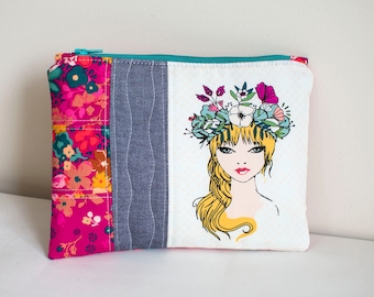 May include: A pink and white zippered pouch with a floral print on one side and a drawing of a woman with a flower crown on the other side.