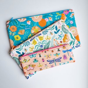 May include: Three zippered pouches with floral and insect patterns. The largest pouch is turquoise with orange and yellow flowers. The medium pouch is white with green leaves and butterflies. The smallest pouch is peach with pink and blue butterflies and dragonflies.