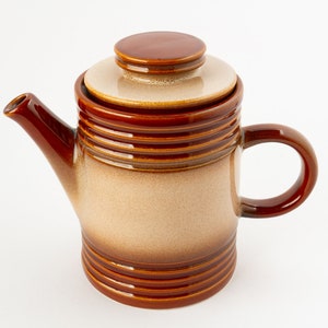 Puede incluir: Una tetera de cerámica marrón y beige con tapa y asa. La tetera tiene un diseño a rayas.