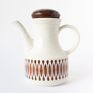 May include: A white ceramic pitcher with a brown lid and a brown geometric pattern. The pitcher has a spout and a handle.