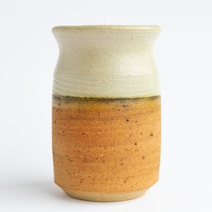 Puede incluir: Un jarrón de cerámica con la parte superior blanca y la inferior marrón. El jarrón tiene una superficie texturizada y una forma redondeada.