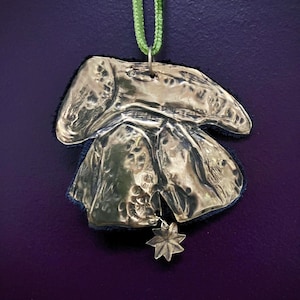 Könnte beinhalten: Ein silberfarbener Anhänger mit strukturierter Oberfläche und Sternanhänger, an einem grünen Band aufgehängt. Der Anhänger befindet sich vor einem dunkelblauen Hintergrund.