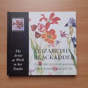 May include: Book cover featuring a painting of flowers in shades of red, orange, and purple. The title is "The Artist at Work in her Studio" and the author is "Elizabeth Blackadder". The subtitle is "Learn the secrets of mastering flower painting and still life".