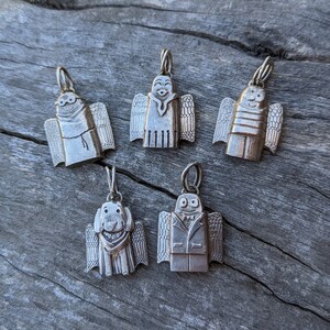 A group shot of the growing collection from artist Jen Van Schmus of her hand carved sterling silver angels shown on a tree limb