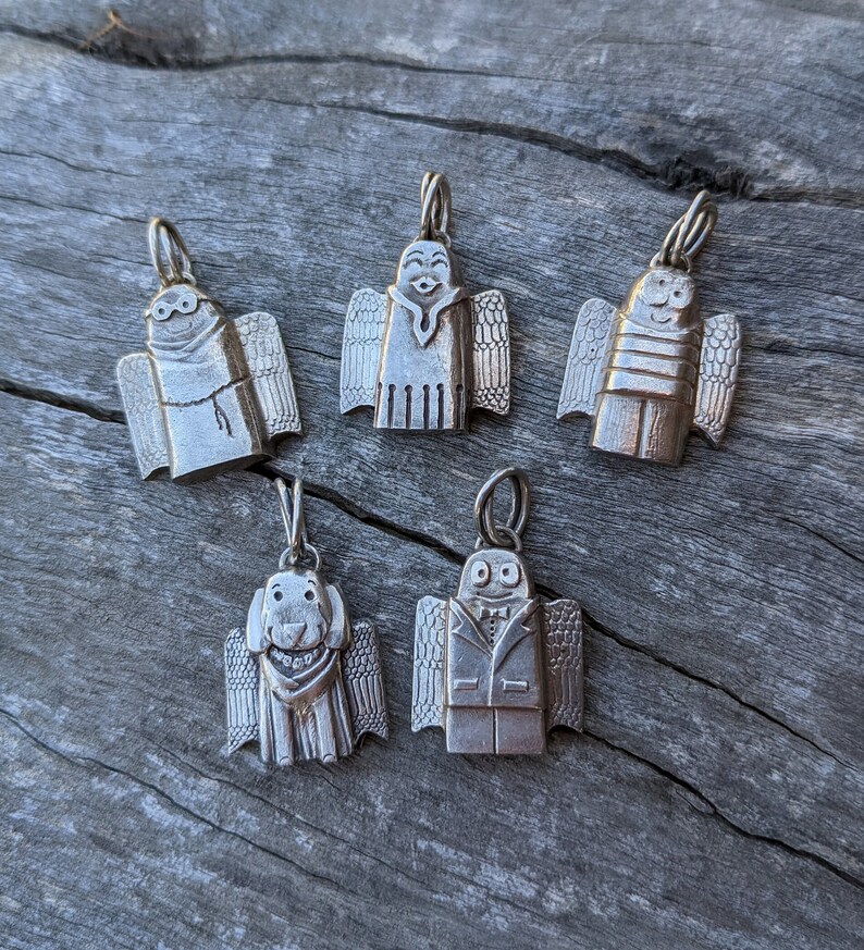 A group shot of the growing collection from artist Jen Van Schmus of her hand carved sterling silver angels shown on a tree limb