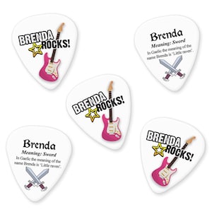 May include: Four white guitar picks with the name Brenda and the text "Brenda Rocks!" printed on them. Each pick features a pink electric guitar and a yellow star. Two of the picks also include the text "Meaning: Sword" and "In Gaelic the meaning of the name Brenda is 'Little raven'."