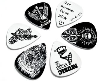 May include: A set of five guitar picks in black and white. Designs include a winged guitar with 'ROCK ROLL FESTIVAL' text, 'Our forever first pick 10-9-27' with a heart, a skeleton, a grim reaper figure, and a gramophone with 'MUSIC STUDIO EST. 2026' text.