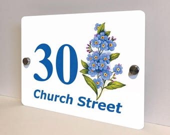 May include: White rectangular house number sign with the number 30 in blue, and the words "Church Street" in blue. A floral illustration of blue flowers with green leaves is on the right side. Two silver mounting screws are visible.