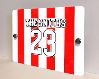May include: Rectangular sign with red and white vertical stripes. The text "THE SMITHS" is at the top, and the number "23" is in the center. The sign is mounted with two silver-colored screws.