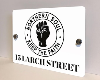 May include: White rectangular sign with the words "NORTHERN SOUL KEEP THE FAITH" encircling a black fist. The sign also displays the address "15 LARCH STREET" in black text. Two silver-colored screws are visible.