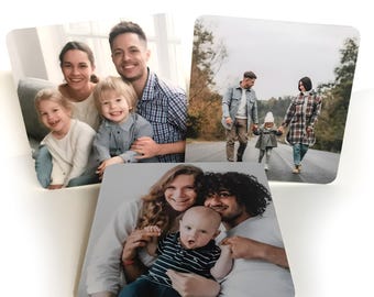 May include: Three square photo prints with rounded corners. Each print features a family portrait. One shows a family of four, another a family of three walking on a road, and the last a family of three with a baby.