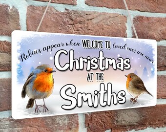 May include: A white wooden sign with a winter scene and two robins. The sign says "Robins appear when welcome to loved ones are near Christmas at the Smiths".