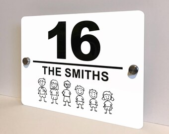 May include: White rectangular house number sign with the number 16 in bold black font. Below the number is the text "THE SMITHS" in black. A black line separates the text from a row of stick figure family members. The sign is mounted with two silver screws.