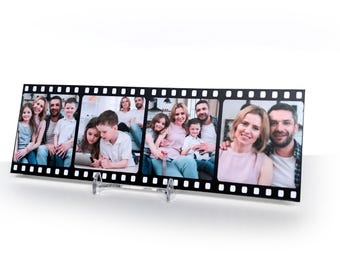 May include: A black film strip photo display with multiple family photos. The display is supported by a clear stand. The photos show families smiling and posing. The film strip has a series of evenly spaced perforations along the top and bottom edges.