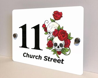 May include: White rectangular house number sign with the number "11" in black. The sign features a graphic of two skulls and red roses. The words "Church Street" are printed in black below the number. Two silver mounting bolts are visible.