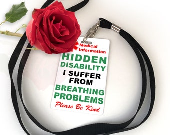 May include: A white medical information badge with the text "HIDDEN DISABILITY I SUFFER FROM BREATHING PROBLEMS Please Be Kind" is attached to a black lanyard. A red rose rests near the badge.