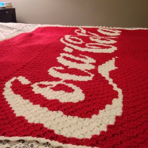 May include: A red crocheted blanket with the word "Coca-Cola" in white yarn.