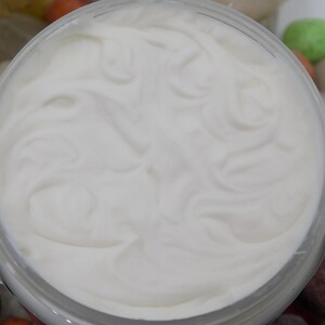 May include: A white cream in a clear glass jar with a white lid. The cream is smooth and has a swirl pattern.