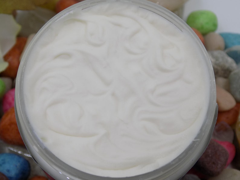 May include: A white cream in a clear glass jar with a white lid. The cream is smooth and has a swirl pattern.