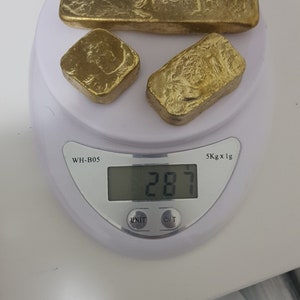 May include: Three gold bars of different sizes are placed on a white digital scale. The scale reads 287. The scale is labeled "WH-B05" and "5Kg x 1g".