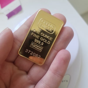 May include: A gold bar with the inscription "CREDIT SUISSE ONE OUNCE FINE GOLD 999.9 ESSAYEUR FONDEUR 372062"