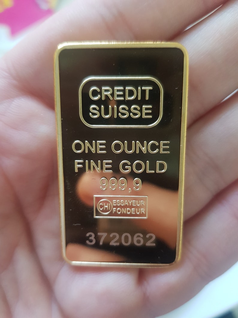May include: A gold bar inscribed with "CREDIT SUISSE" and "ONE OUNCE FINE GOLD 999.9". The bar also features a stamp reading "ESSAYEUR FONDEUR" and the number "372062".