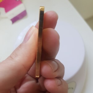 May include: A close-up of a gold bar, held in a hand. The bar is rectangular and has a smooth, shiny surface.