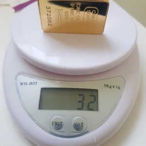 May include: A gold bar on a white digital scale. The scale reads 32 grams. The gold bar is labelled "CRED SUISSE ONE OUNCE FINE GOLD 999.9 372062".