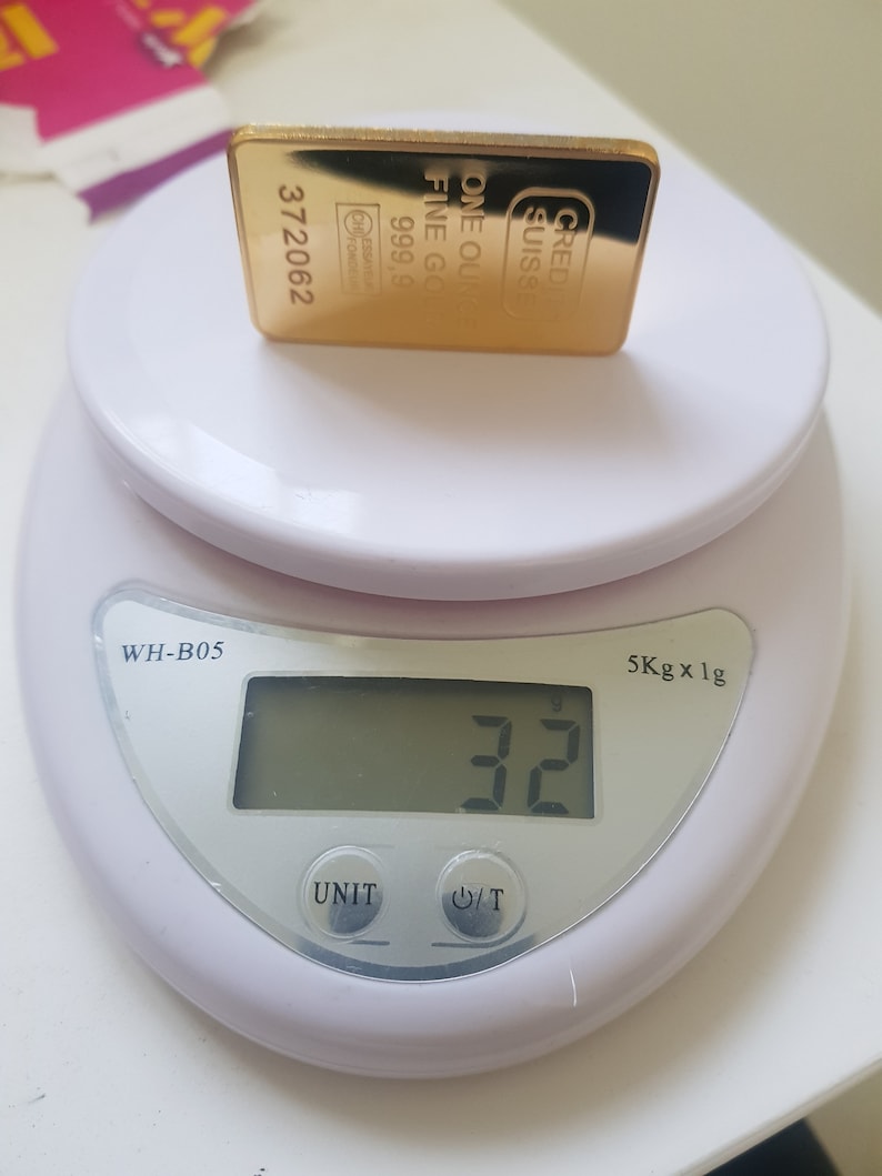 May include: A gold bar on a white digital scale. The scale reads 32 grams. The gold bar is labelled "CRED SUISSE ONE OUNCE FINE GOLD 999.9 372062".