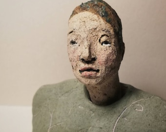 May include: A ceramic bust sculpture of a person with a green and brown head and a green torso. The person has a neutral expression and is looking slightly to the right.