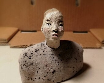 May include: A ceramic sculpture of a person's head and shoulders. The sculpture is painted white with black speckles and has a realistic face.