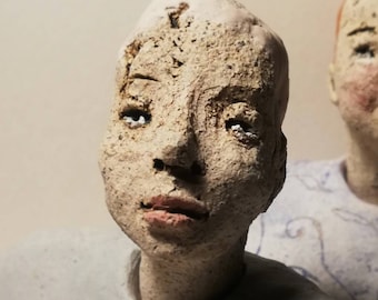 May include: Close-up of a ceramic sculpture of a person's face. The sculpture is made of a rough, textured material and has a neutral expression. The person's eyes are closed and their lips are slightly parted.