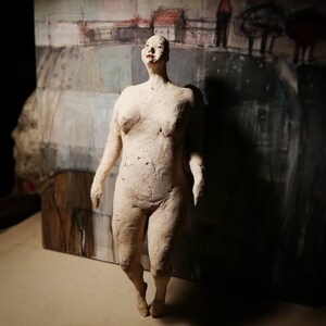 May include: A white ceramic sculpture of a person standing with their head tilted back and their arms at their sides.