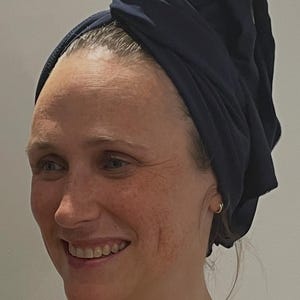 May include: A dark navy blue hair wrap made of smooth fabric, secured in a twisted style on top of the head. The wrap covers the hair completely, featuring a simple, solid-coloured design with a soft texture and a secure, folded construction.